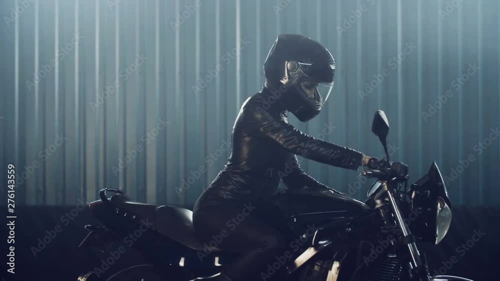 Stylish brutal biker girl in a black glossy helmet and black leather jacket is sitting on his bike. Neon illumination. Preparation in the night races. Moto service. Frame for the film.