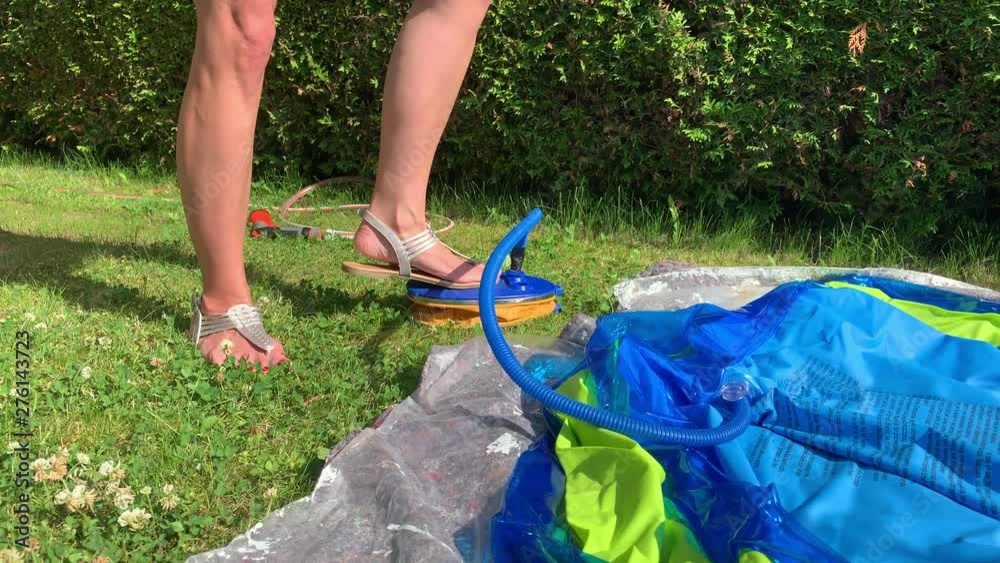 [Pan] Woman using manual air pump to fill inflatable pool with air. Person steps on foot pump to inflate swimming pool.