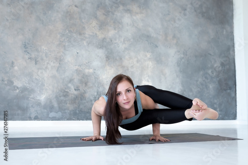 Young european woman with long hair holding arm balance in Astavakrasana yoga pose. Full length studio shot