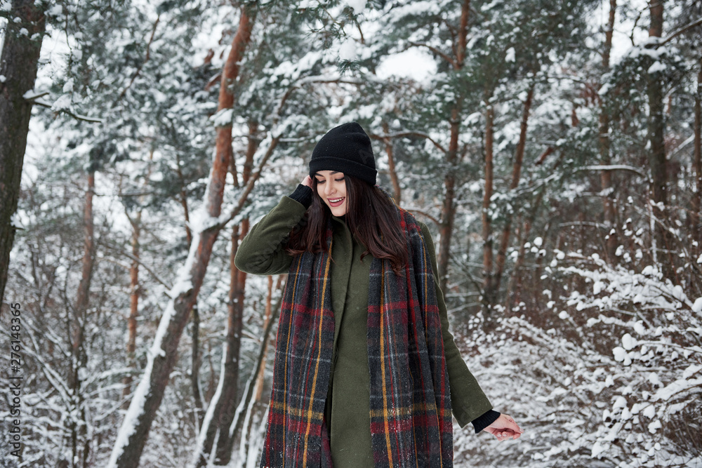 Holidays season. Cheerful young girl in warm clothes have a walk in the winter forest at daytime