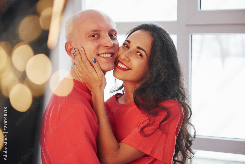 Feels awesome to be together. Cheerful couple standing near the window, smiling and looking into the camera Feels awesome to be together. Cheerful couple standing near the window, smiling and looking into the camera
