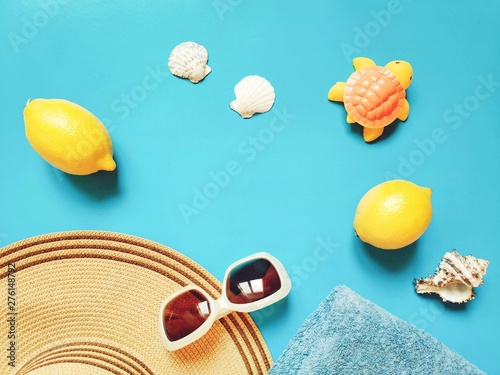 Summer travel mockup and banner. Women's sun beach hat, lemons, towel, seashells and rubber toy turtle on a blue background. Flat lay composition photography, top view picture