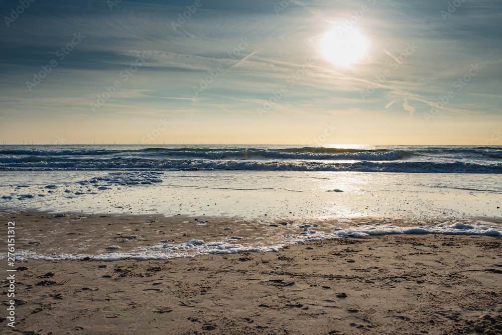 Beautiful coast of the North Sea under the soft sun in the evening, colorful panorama with windmills on the horizon in the distance