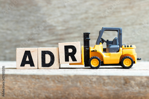 Toy forklift hold letter block r to complete word ADR (Abbreviation of Adverse drug reaction) on wood background photo