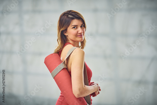 Beautiful Caucasian woman dressed in red outfit holding exercise mat. Yoga exercise concept.