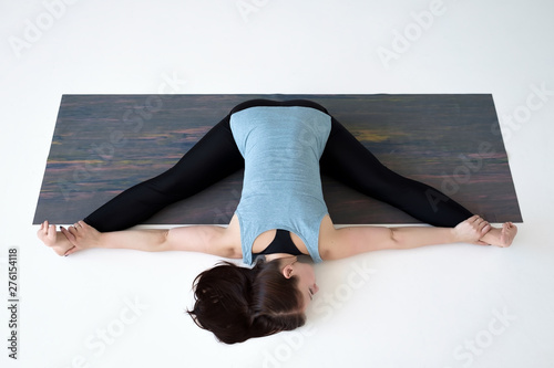 Caucasian woman doing yoga splits upavistha konasana on fitness mat. Full length studio shot. Top view on white floor photo