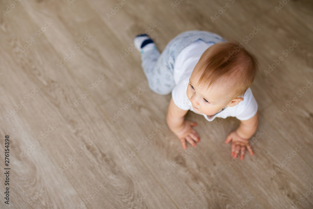 Cute little baby boy lying on hardwood and smiling. Child crawling over wooden parquet and looking up with happy face. View from above. Copyspace - obrazy, fototapety, plakaty 