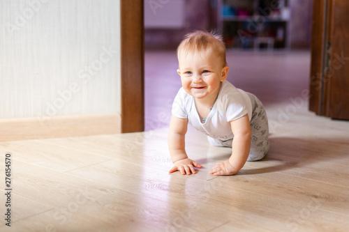 Cute little baby boy lying on hardwood and smiling. Child crawling over wooden parquet and looking up with happy face. View from above. Copyspace