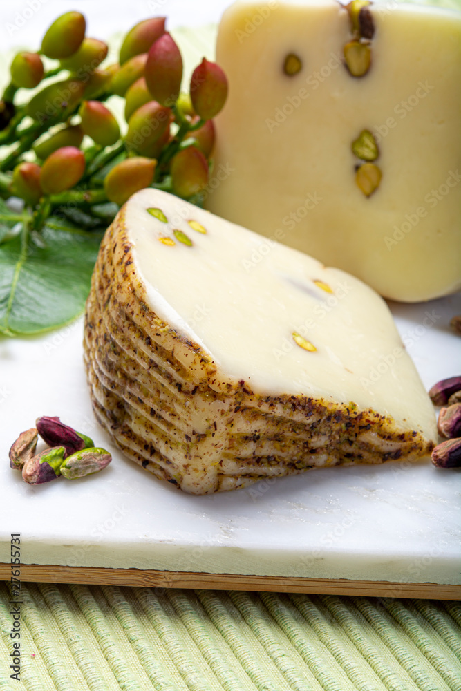 Italian provolone or provola cheese made in Sicily with tasty green Bronte pistachio nuts served on white marble plate close up