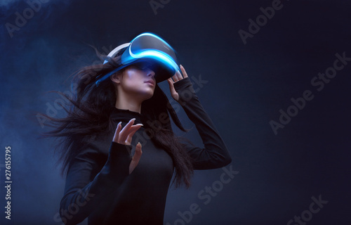 Beautiful woman with flowing hair in futuristic dress over dark background. Girl in glasses of virtual reality. Augmented reality, science, future technology, robots and people concept. VR.