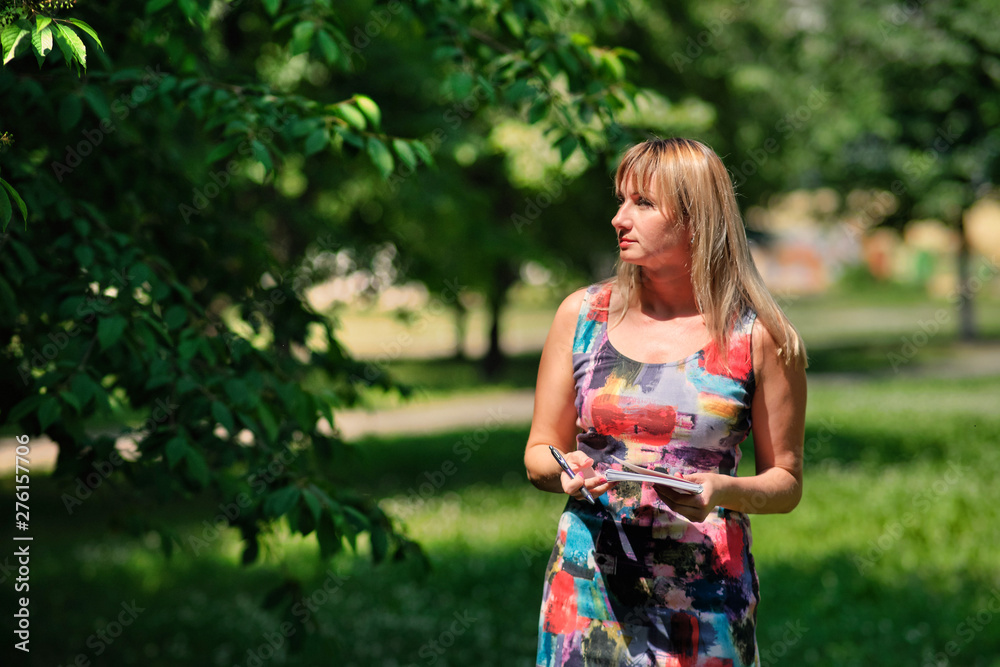 beautiful blonde girl walks in a summer park with, with a notebook and pen beautiful blonde girl walks in a summer park with, with a notebook and pen