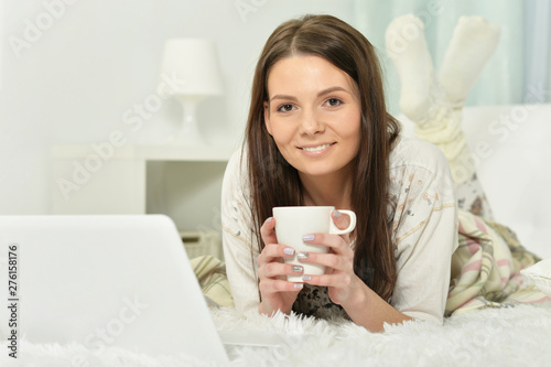 Young woman lying on bed with cup of coffee