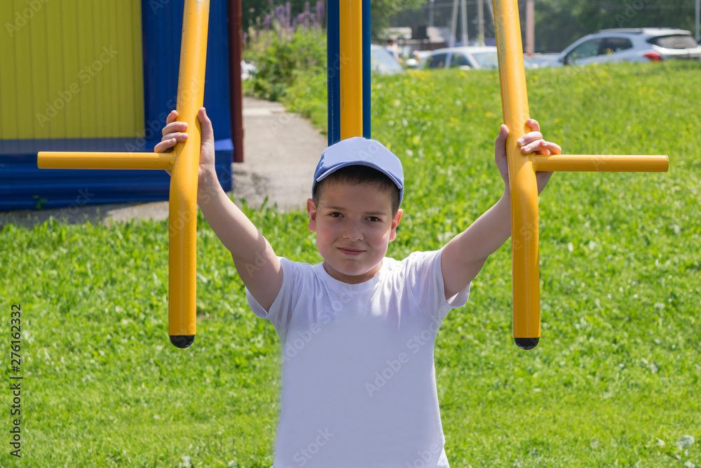 Fototapeta premium The boy is engaged in the yard on the street simulator. The child smiles while doing sports.