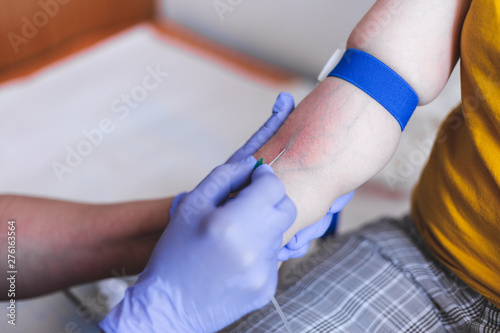 Nurse with blue gloves holding the tight the hand of a patient while inserting the needle into his vein in the hospital     Female doctor drawing blood from a young person   s arm