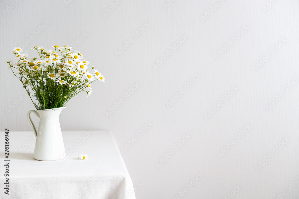 Bouquet of daisy-chamomile flowers in white vase on the table on white background. Copy space.