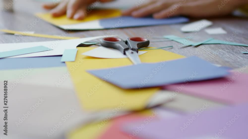 Tilt up close up shot of hands of unrecognizable female decorator using glue sticks to make collage from pieces of colored paper