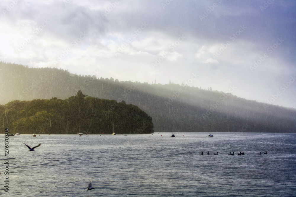 A stunning view of Lake Windermere during a light downpour. The sun's rays filter through the clouds and illuminate some points of the lake. Lake District National Park. Cumbria, England, UK.