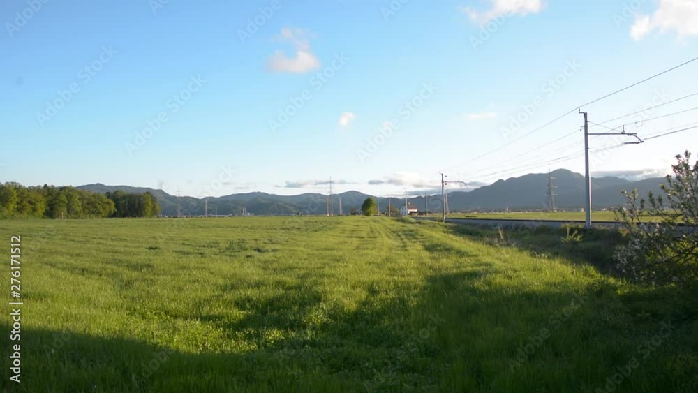 Freight train comes into view on train tracks cutting through a rural countryside area filled with grass fields. Freight train comes into view on train tracks cutting through a rural countryside area filled with grass fields.