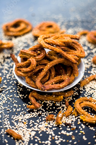 Famous Indian snack in a glass plate on the wooden surface along with raw sesame seeds or til spread on the surface. photo