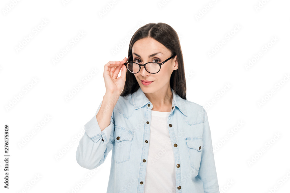 curious brunette girl in glasses and denim jacket looking at camera isolated on white