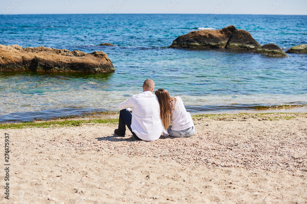 Couple in love hugging on a tropical beach with a turquoise water and rocks in the background