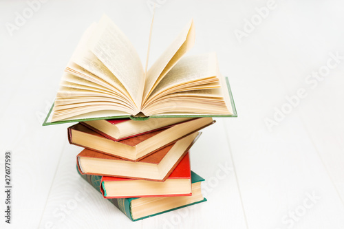 stack of books lies on a white wooden table, one book is opened, with text.