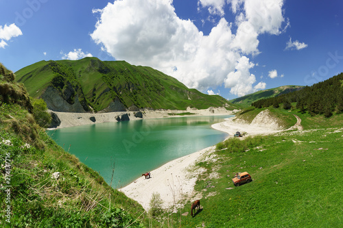 Beautiful view of the mountain lake Kezenoi am in Botlikh district of the Republic of Dagestan. On the shore grazing horses. Juicy greens in early summer photo