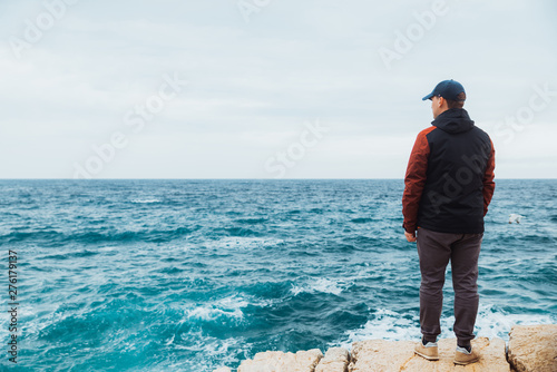 man standing on the edge looking forward at sea.