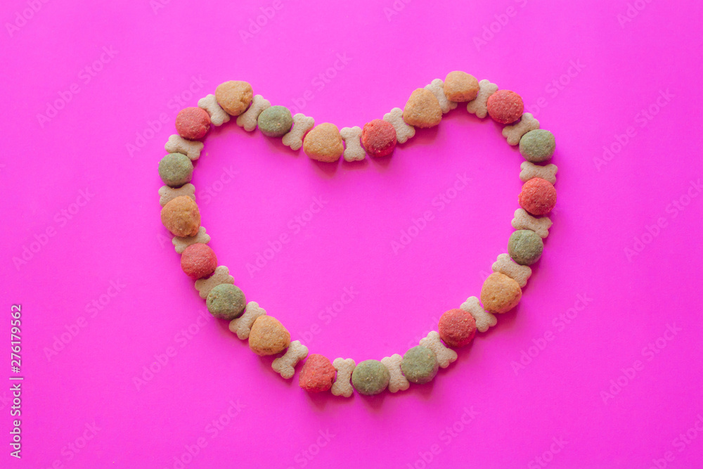Obraz premium Creative valentines concept photo of Dog food and a heart be lovely on pink background.