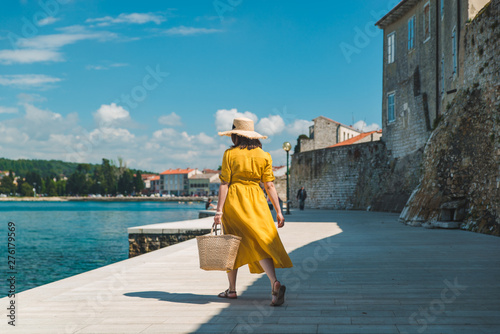 woman walking by sea quay in summer day in yellow sundress © phpetrunina14