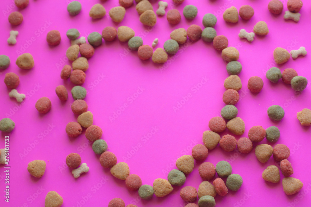 Creative valentines concept photo of Dog food and a heart be lovely on pink background.