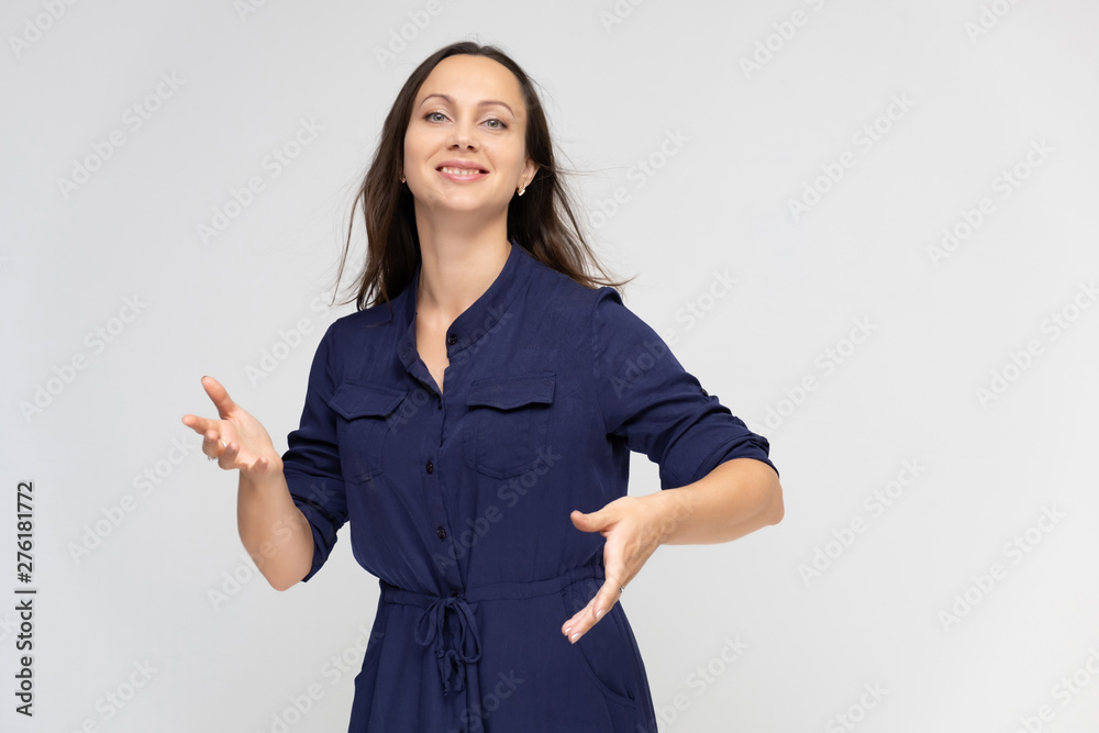 Portrait of a young pretty brunette woman of 30 years old in a simple plain blue dress with dark hair. Standing right in front of the camera, talking, showing hands, demonstrating emotions. Portrait of a young pretty brunette woman of 30 years old in a simple plain blue dress with dark hair. Standing right in front of the camera, talking, showing hands, demonstrating emotions.