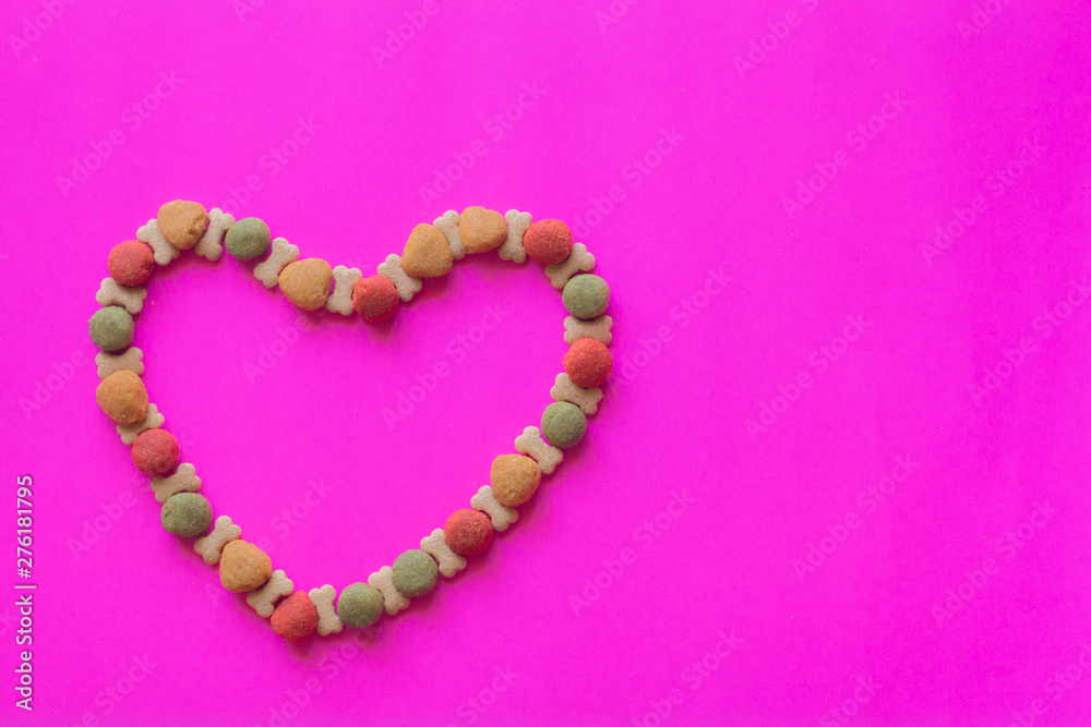 Creative valentines concept photo of Dog food and a heart be lovely on pink background.