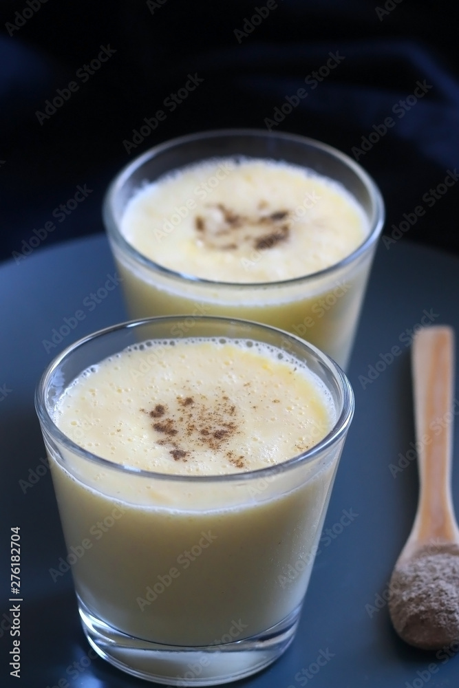 Two glasses of refreshing mango lassi drink, decorated with cardamom. Dark background, selective focus. Two glasses of refreshing mango lassi drink, decorated with cardamom. Dark background, selective focus.