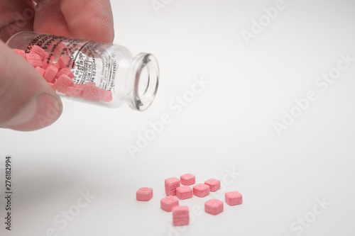 Small vial with pink pills in the hand. White background.