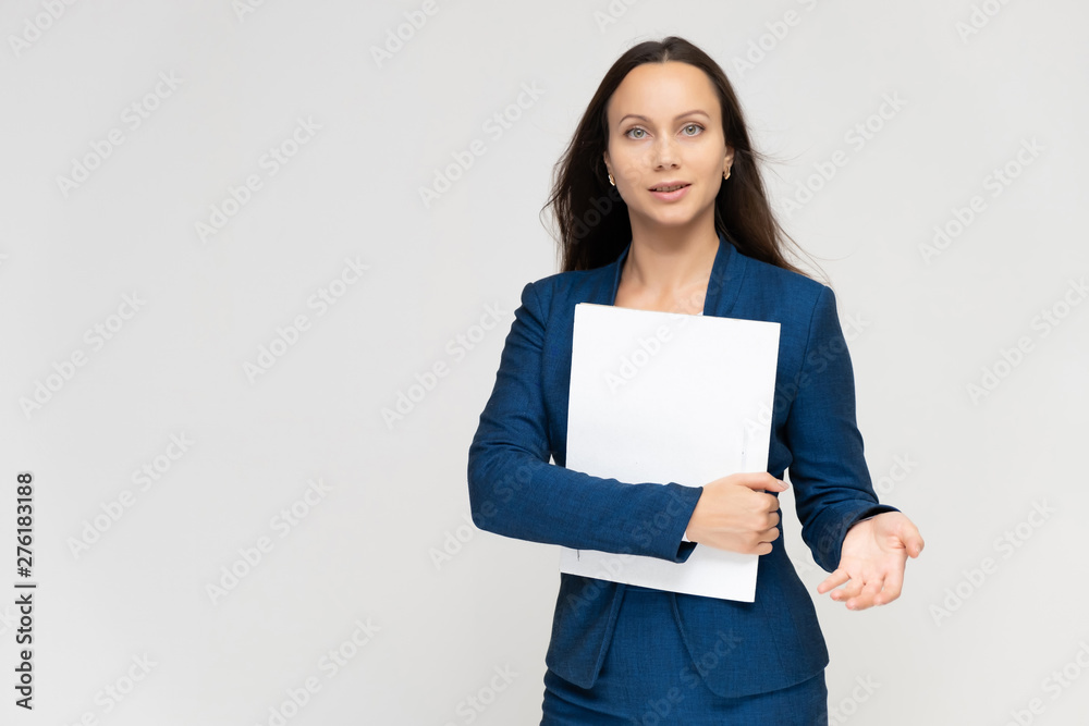 Portrait of a young pretty brunette manager woman of 30 years in a business blue suit with beautiful dark hair. Standing with a folder on a white background, talking, showing hands, with emotions Portrait of a young pretty brunette manager woman of 30 years in a business blue suit with beautiful dark hair. Standing with a folder on a white background, talking, showing hands, with emotions