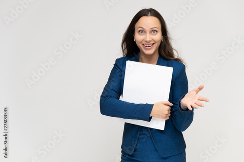 Portrait of a young pretty brunette manager woman of 30 years in a business blue suit with beautiful dark hair. Standing with a folder on a white background, talking, showing hands, with emotions