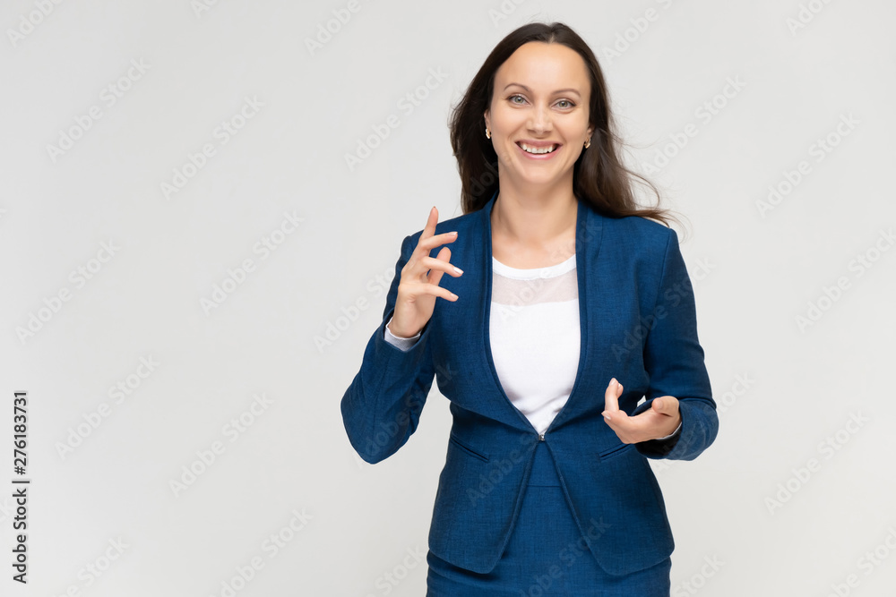 Portrait to the waist a young pretty brunette manager woman of 30 years in a business blue suit with beautiful dark hair. Standing on a white background, talking, showing hands, with emotions. Portrait to the waist a young pretty brunette manager woman of 30 years in a business blue suit with beautiful dark hair. Standing on a white background, talking, showing hands, with emotions.