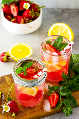 Lemonade with fresh srtawberries, lemons and ice on a light stone or slate table.