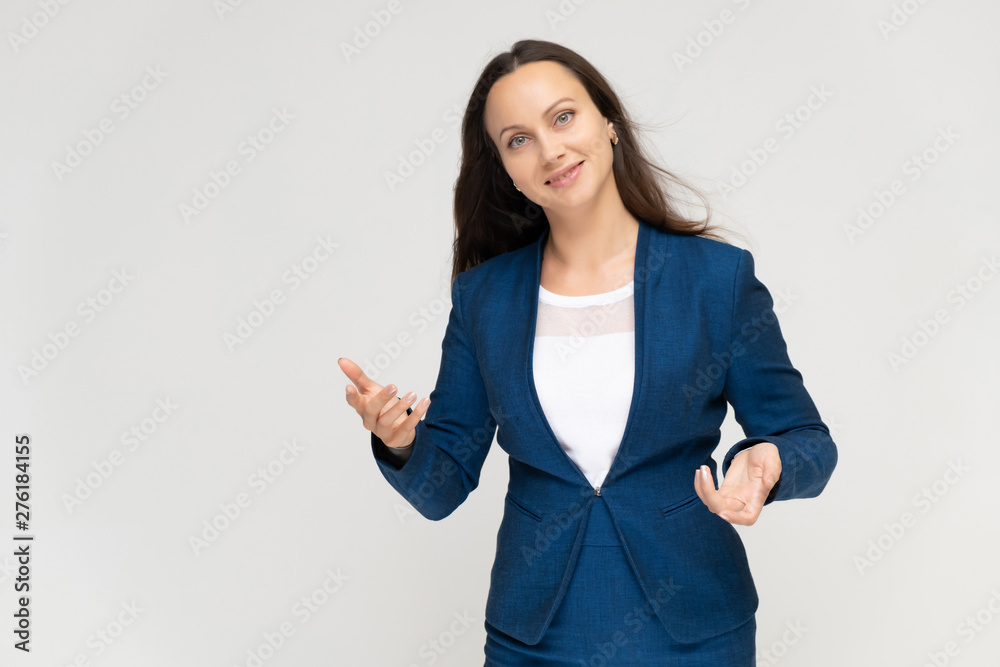 Portrait to the waist a young pretty brunette manager woman of 30 years in a business blue suit with beautiful dark hair. Standing on a white background, talking, showing hands, with emotions. Portrait to the waist a young pretty brunette manager woman of 30 years in a business blue suit with beautiful dark hair. Standing on a white background, talking, showing hands, with emotions.