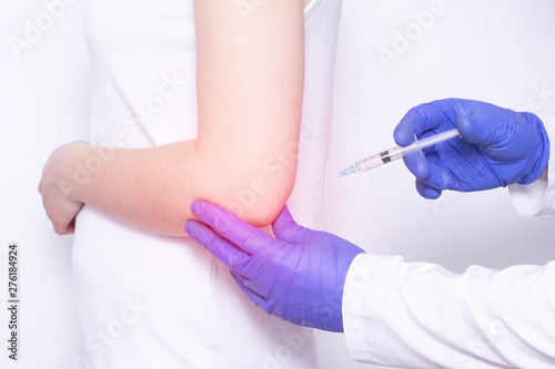 Doctor injects blockade of chondroprotector and ozone therapy to a young girl in a sore elbow joint, close-up, corticosteroid photo