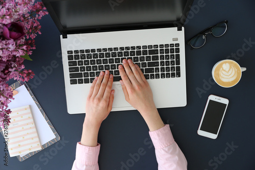 Feminine freelance workspace concept. Woman's hands typing on white laptopp with black keyboard, desk with matte blue table top. Freelance blogger writing an article. Close up, copy space for text. photo