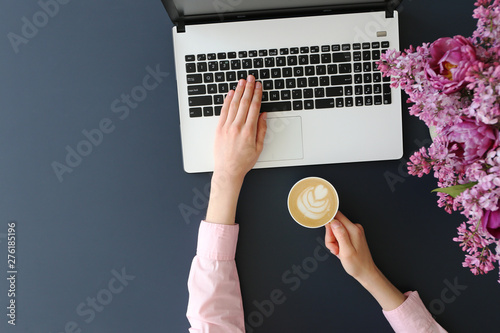 Feminine freelance workspace concept. Woman's hands typing on white laptopp with black keyboard, desk with matte blue table top. Freelance blogger writing an article. Close up, copy space for text. photo