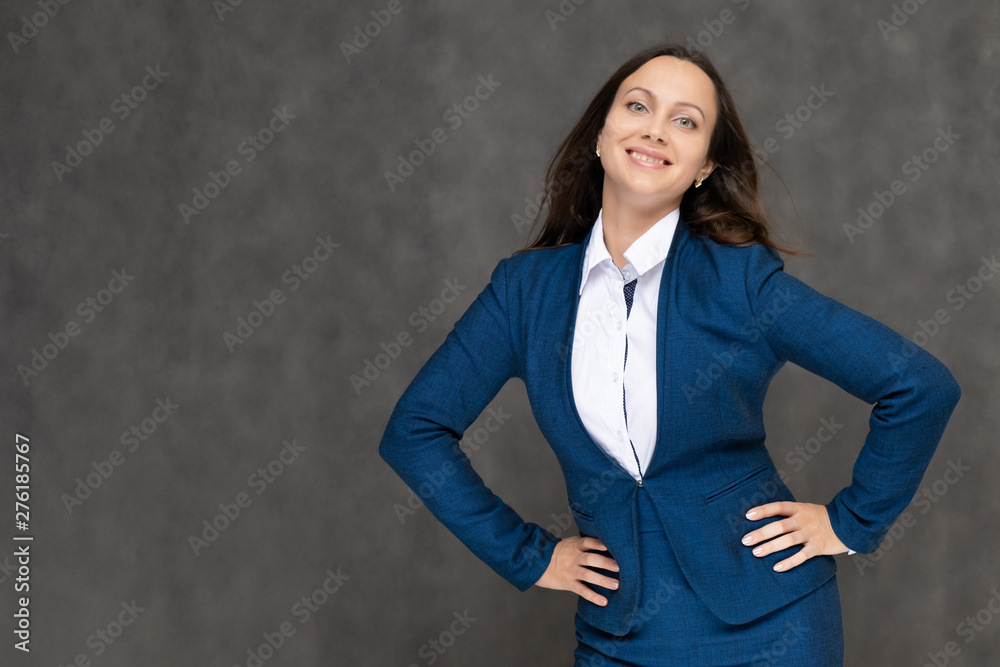 Portrait to the waist a young pretty brunette manager woman of 30 years in a business blue suit with beautiful dark hair. It is standing on a gray background, talking, showing hands, with emotions Portrait to the waist a young pretty brunette manager woman of 30 years in a business blue suit with beautiful dark hair. It is standing on a gray background, talking, showing hands, with emotions