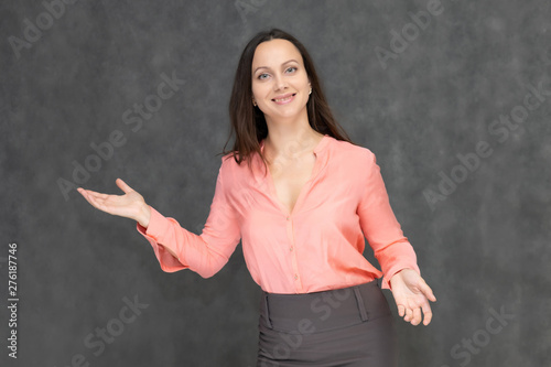 Portrait to the waist a young pretty brunette manager woman of 30 years in business clothes with beautiful dark hair. It is standing on a gray background, talking, showing hands, with emotions