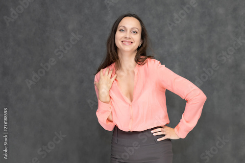 Portrait to the waist a young pretty brunette manager woman of 30 years in business clothes with beautiful dark hair. It is standing on a gray background, talking, showing hands, with emotions