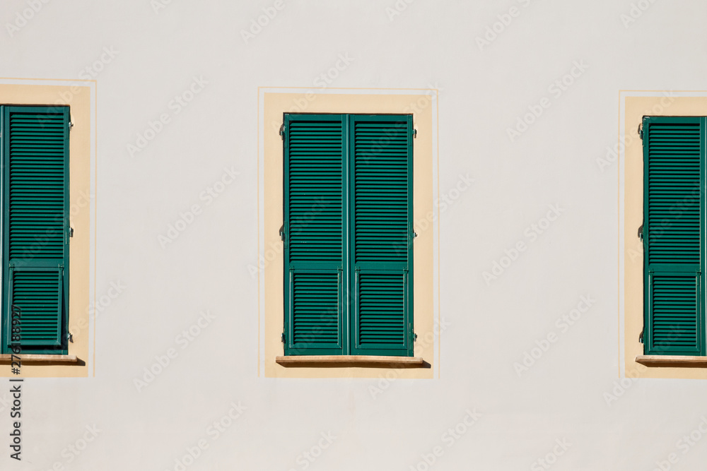 three green wooden window with shutters in yellow frame on white wall