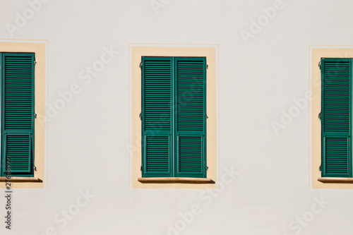 three green wooden window with shutters in yellow frame on white wall © ksenija1803z