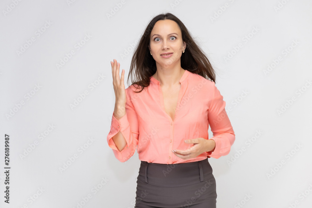 Fototapeta premium Portrait to the waist a young pretty brunette manager woman of 30 years in business clothes with beautiful dark hair. Standing on a white background, talking, showing hands, with emotions.