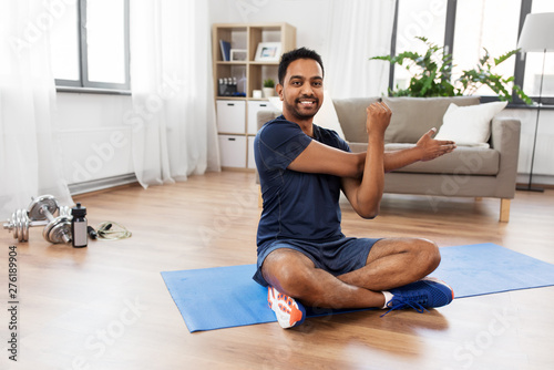 sport, fitness and healthy lifestyle concept - indian man training and stretching arm at home